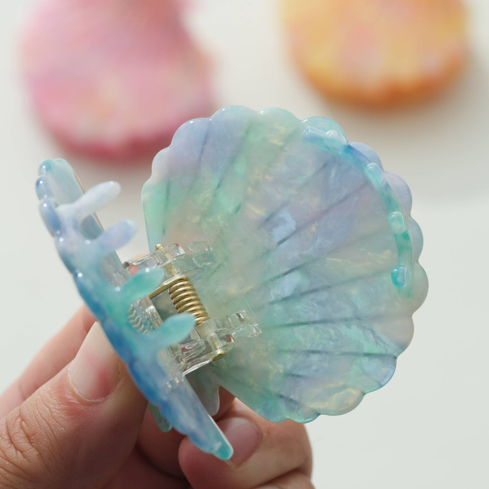 Shell-shaped hair clip held by a hand with a blurred background