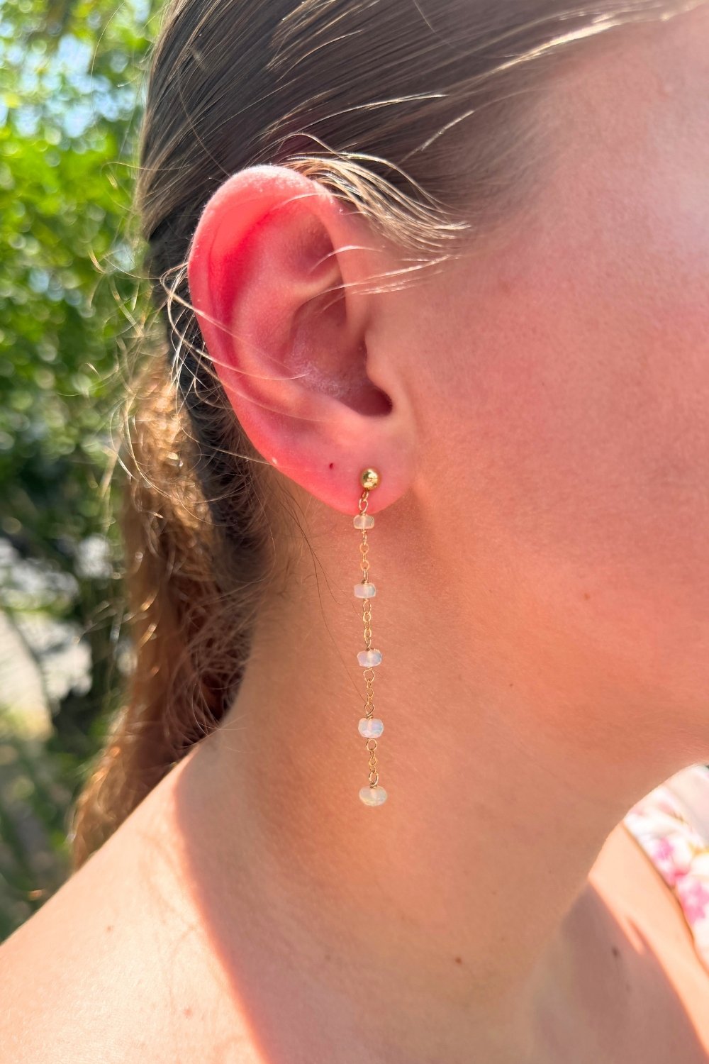 Close-up of a person wearing a dangling opal oasis earring with a blurred natural background