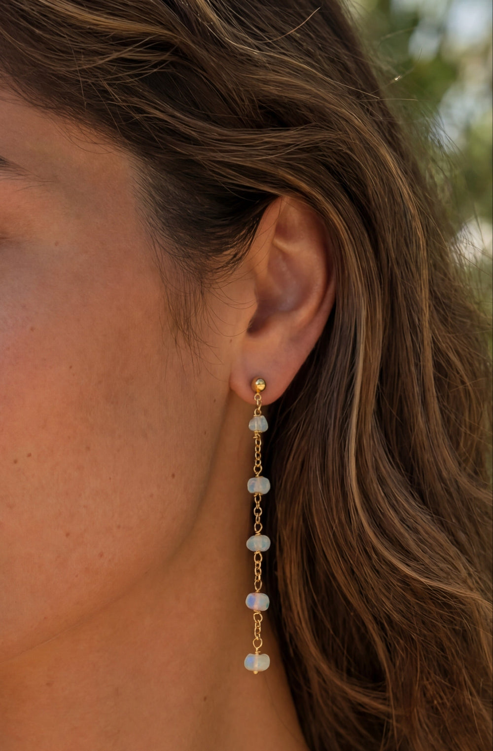 Woman wearing gold earrings with opal beads outdoors