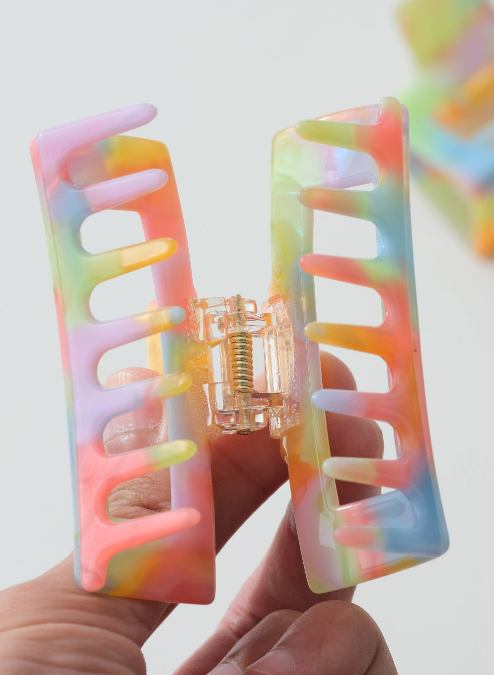 Colorful tie-dye hair clip held by a hand against a light background