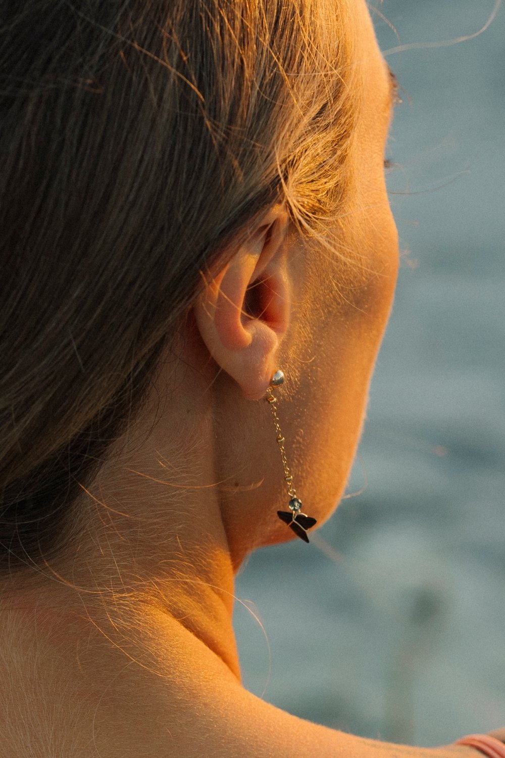 Close-up of a person wearing a riptide shark tooth earring with a blurred water background