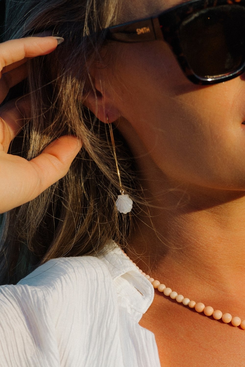 Close-up of a person wearing scallop shell threader earrings with a blurred background