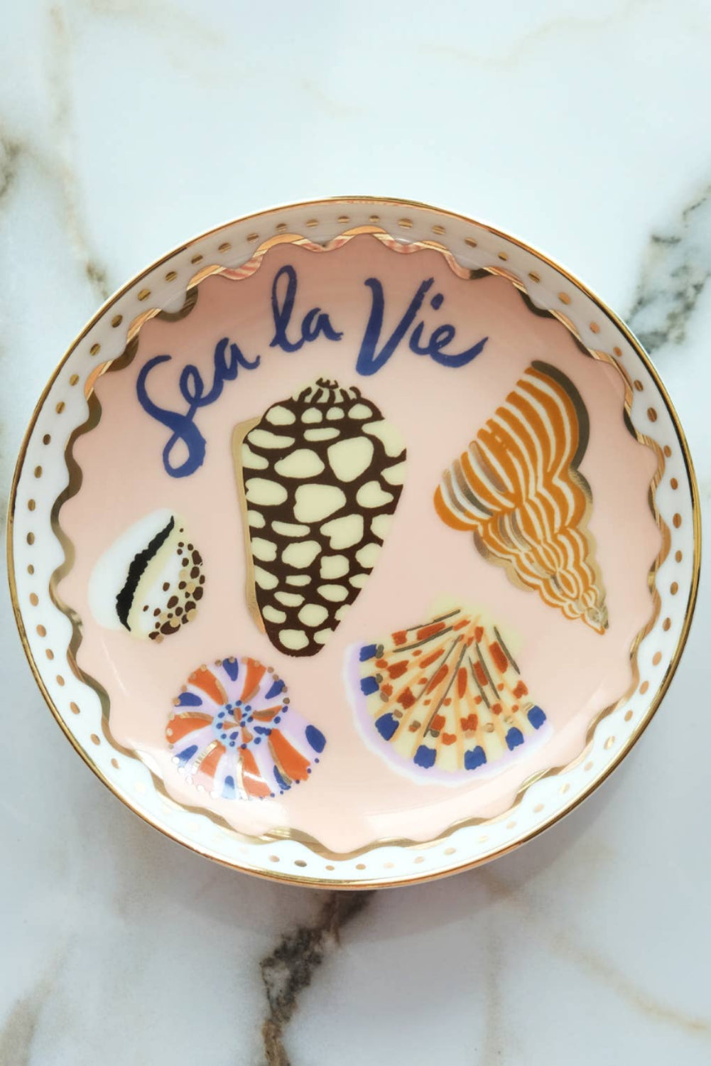 Decorative plate with shell designs and 'Sea la Vie' text on a marble background