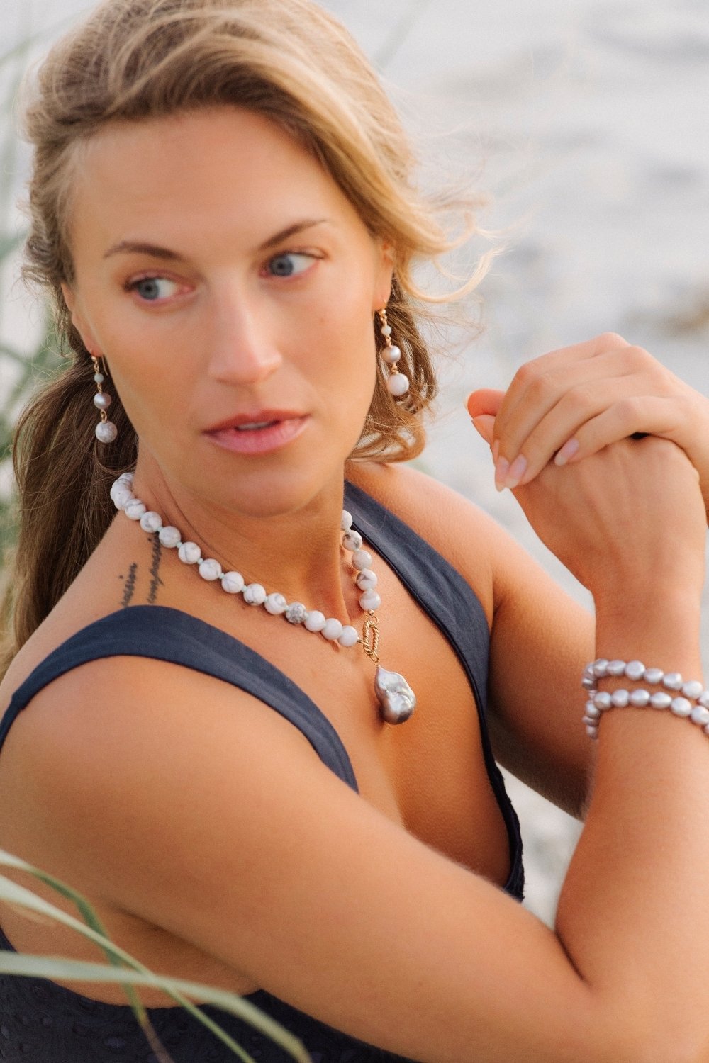 Woman wearing seamist necklace with large pearl pendant and a blurred natural background