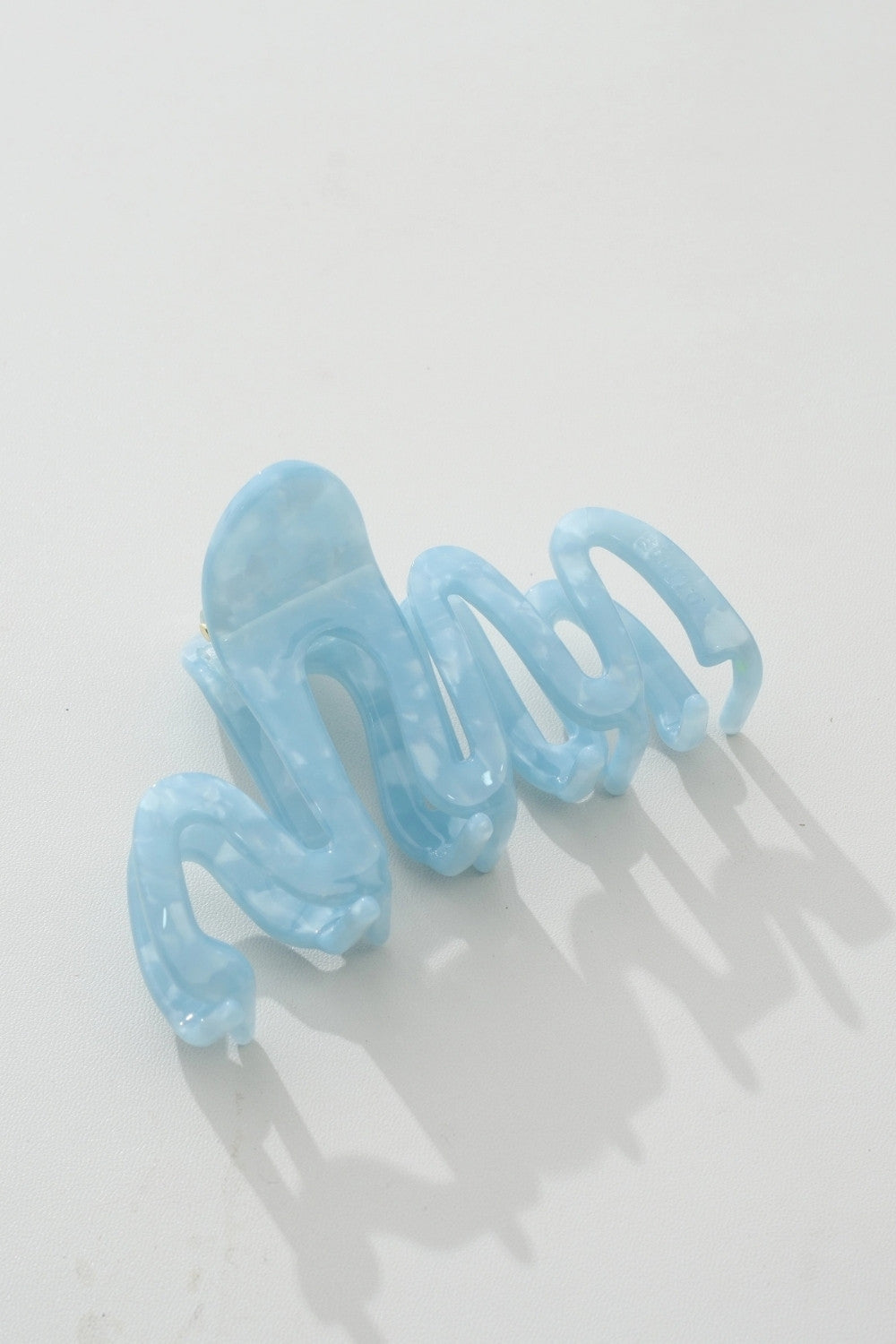 A single light blue translucent spiral hair claw clip on a clean white background with soft shadows.
