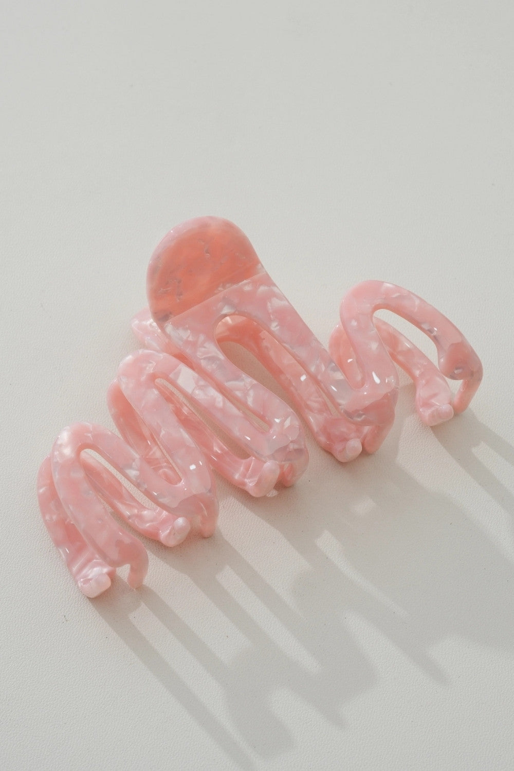 A single light pink translucent hair claw clip with a marbled pattern, photographed on a clean white surface with soft shadows.