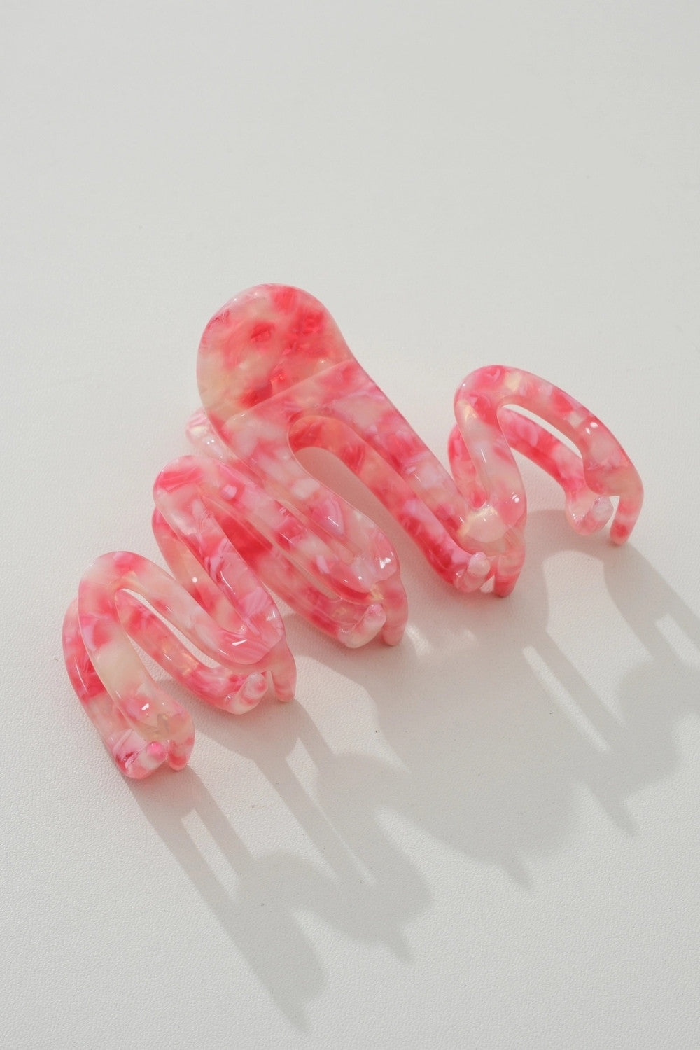 A set of four translucent pink and white marbled spiral hair claw clips arranged on a light gray background.