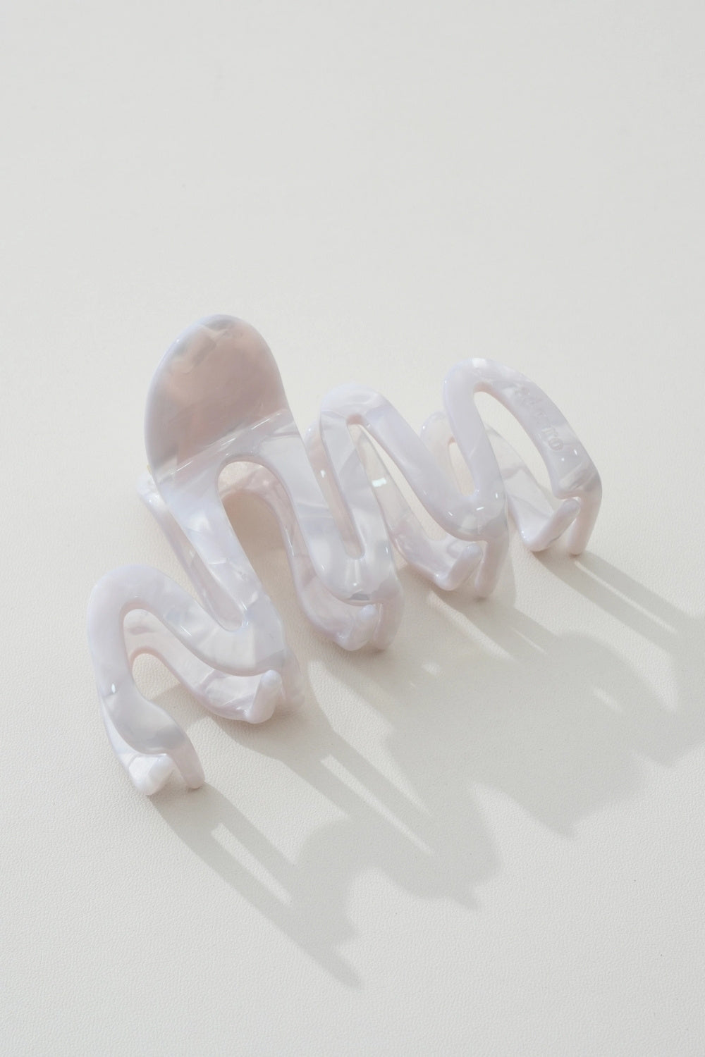 A translucent white resin claw hair clip with a wavy, organic design, photographed on a clean off-white background with soft shadows.